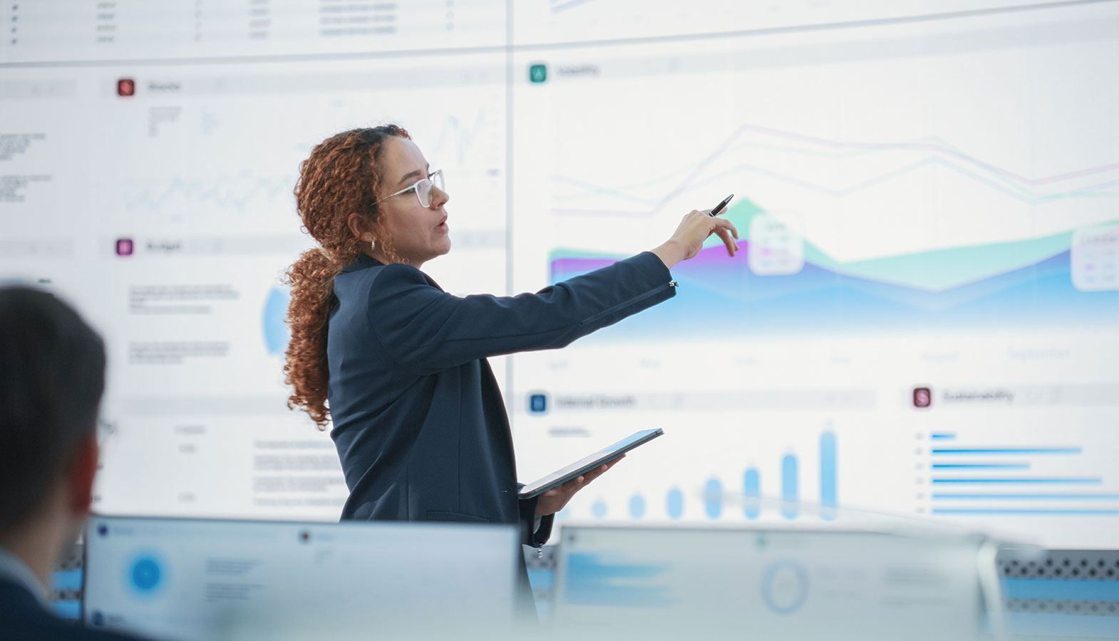 A diverse group of team members is engaged in a business meeting, collaboratively reviewing charts and planning documents on a table, while discussing strategies for improving search engine optimization and utilizing AI tools for better search rankings. The atmosphere is focused and productive, reflecting a commitment to enhancing their digital marketing efforts.